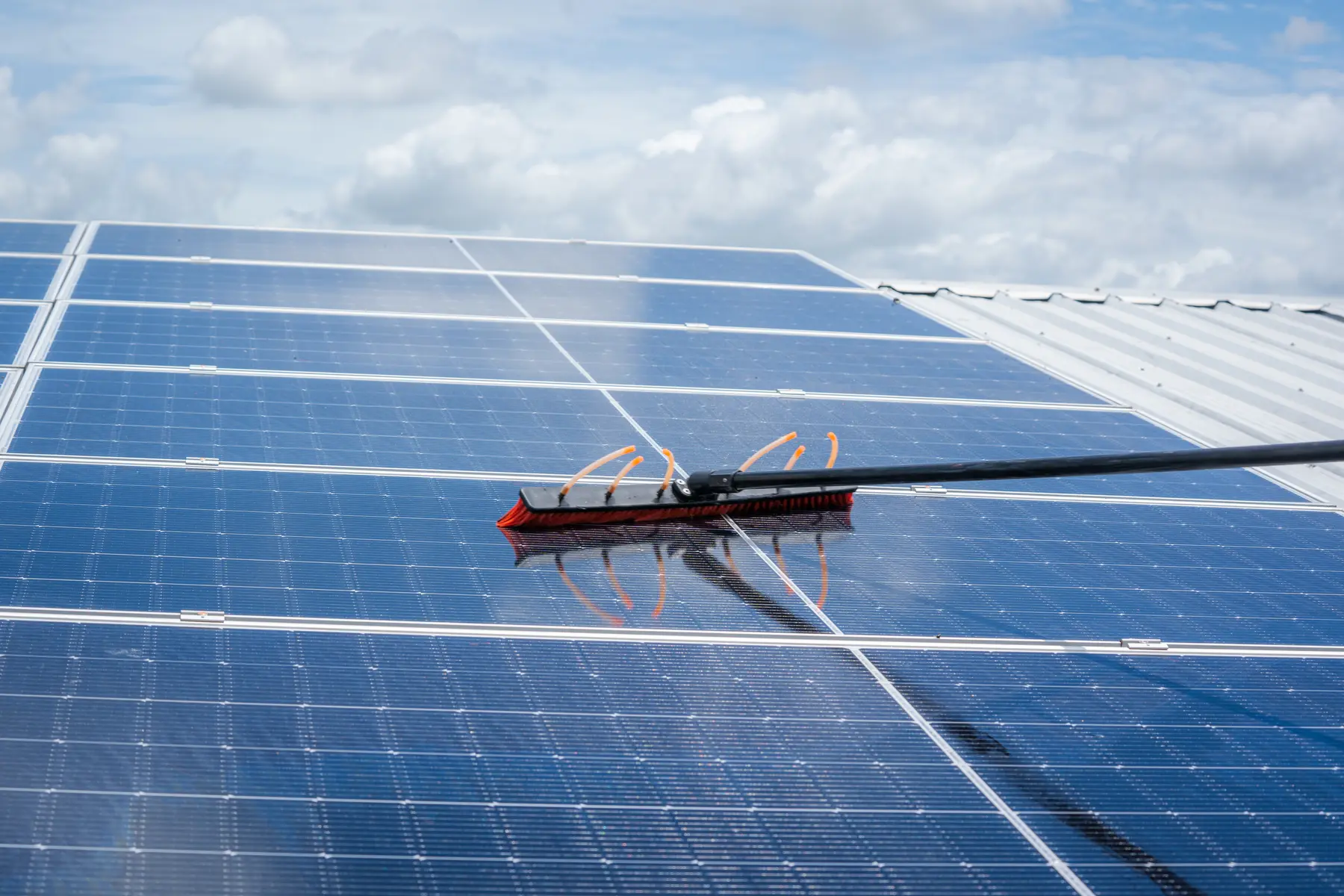 Cepillo de cerda suave sobre una hilera de placas solares con el cielo nublado de fondo